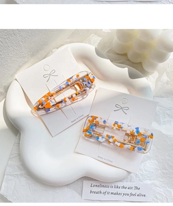 Close-up of acetic acid hair clips with colorful glitter sequins on white ceramic plate