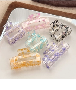Macro detail of six colorful acrylic hair claws with embedded flecks in a ceramic dish