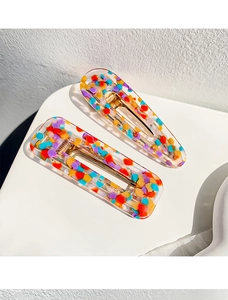 Detailed view of two colorful acetate hair clips with vibrant confetti dots and gold metal base
