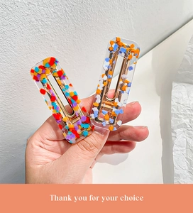 Close-up of resin hair clips featuring colorful floral textures and golden metal duckbill clips