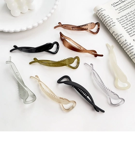 Detail view of colorful matte and glossy banana hair clips on a white ceramic tray