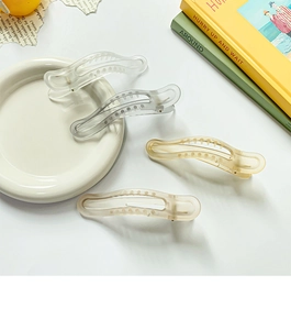 Close-up of four gradient matte banana hair clips on a white ceramic tray with props