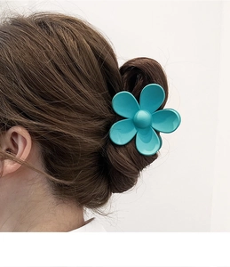 Detailed view of a cyan flower hair claw clip securing a bun on brown wavy hair