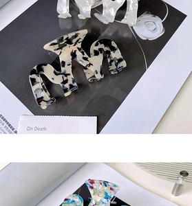 Close-up of large acetate hair claw clips in marble and floral patterns on magazine background