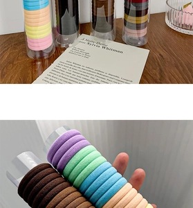 Detail of colorful elastic hair bands stored in a clear cylinder container on a wood table