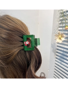 Détail d'une pince à cheveux verte scintillante avec un Père Noël 3D sur cheveux bruns