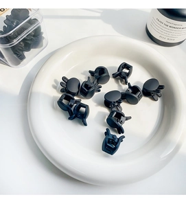 Detailed view of black matte mini hair claws scattered on a white ceramic plate
