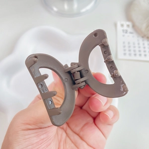 Brown matte hollow D-shaped hair claw clip held by hand for a minimalist Korean style look