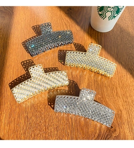 Close-up of four large rhinestone hair claws in gold and silver on a wooden surface