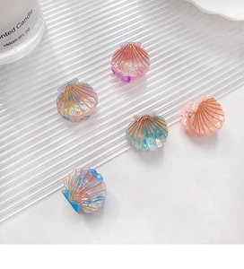 Detail showing five colorful shell-shaped mini hair clips on a white textured background