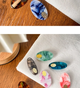 Detail view of oval acetate hair clips with marble texture and golden metal logo
