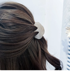 Gros plan d'une pince à cheveux en acrylique marbré crème sur cheveux ondulés bruns