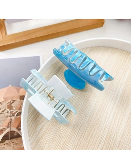 Detail view of two sky blue acrylic hair claws on a decorative plate for beach styling