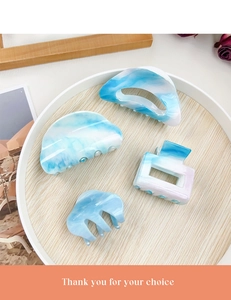 Detailed view of four sky blue marble patterned acrylic hair claws in a wooden tray