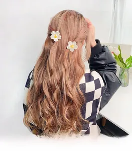 Detail of two white daisy flower hair claws styled on a woman's long wavy hair