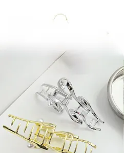 Dettaglio delle grandi mollette per capelli ondulate in oro e argento con perle