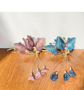 Detail of embroidered butterfly hair clip with golden tassels and gemstone on wood table