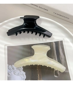 Gros plan de deux grandes pinces à cheveux en acétate noir et blanc nacré sur une assiette