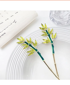 Detailed view of two gold bamboo hair sticks with green enamel leaves on a white plate