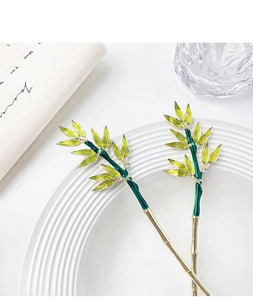 Detail of gold bamboo hairpins with green enamel leaves on a white porcelain plate
