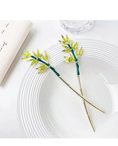 Detail of two golden bamboo hairpins with green enamel leaves on a white ceramic plate