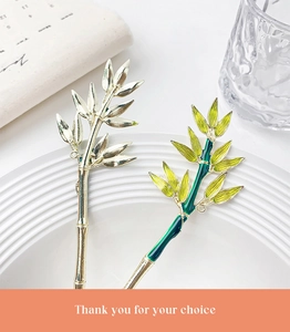 Macro detail of high-quality metal bamboo hairpins with green enamel leaves on a white tray