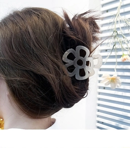 Détail d'une pince à cheveux fleur grise sur cheveux bruns avec motif ajouré à cinq pétales