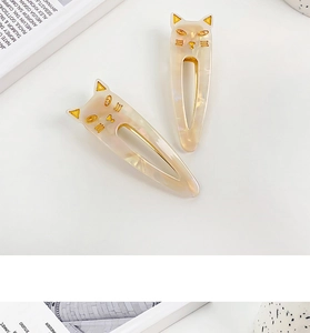 Close-up of two cream cat-shaped hair clips with gold accents and pearlescent finish