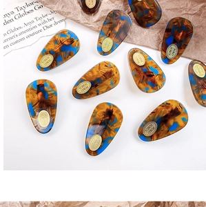 Detail of droplet acetate hair clips with brown and blue tortoiseshell patterns and gold logo