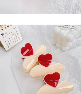 Détail de trois pinces à cheveux crème avec coeurs rouges sur fond blanc texturé