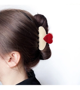Détail d'une pince à cheveux crème avec cœur rouge sur un chignon élégant pour femme