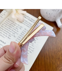 Detail of pink marble acetate hair clip with golden metal bar on an open book