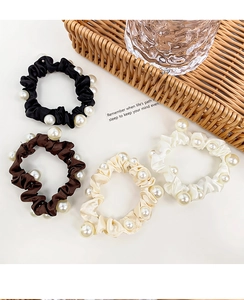 Detailed view of four elegant satin pearl scrunchies in neutral colors on a white base