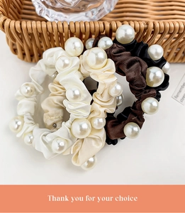 Close-up of elegant satin scrunchies with large pearl accents in neutral tones
