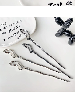 Close-up of minimalist silver wave hairpins with a polished mirror finish on a desk