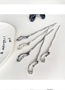 Macro view of four minimalist silver metal hair sticks with fluid wave-like design