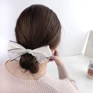 Elegant off-white sequined bow hair tie with black edge shown on a low bun hairstyle