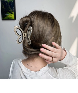 Detail showing a golden metal butterfly hair claw clip with rhinestones on a model
