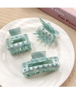 Détail macro de trois pinces à cheveux en acétate vert menthe avec strass brillants sur assiette