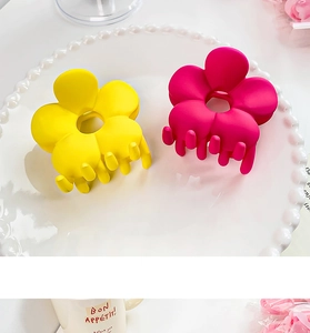 Gros plan de pinces à cheveux florales mates jaunes et rose rouge sur un plat blanc