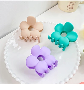 Trois pinces à cheveux fleur mates aux tons pastels présentées sur une assiette blanche