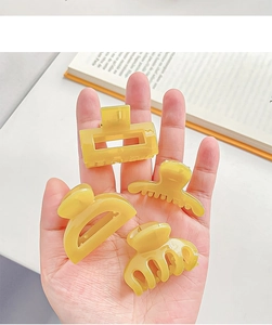 Détail de quatre mini pinces à cheveux jaune vif en résine mate tenues à la main