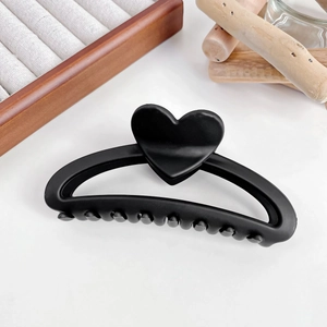 Détail d'une pince à cheveux mate noire de 13cm avec cœur sur fond en bois naturel