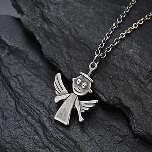 Close-up of vintage silver angel pendant with textured finish on dark rock background