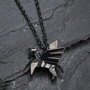Minimalist black origami Pegasus pendant necklace on textured dark stone surface