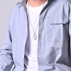 Close-up of a silver astronaut pendant necklace with blue accents on a stylish male model