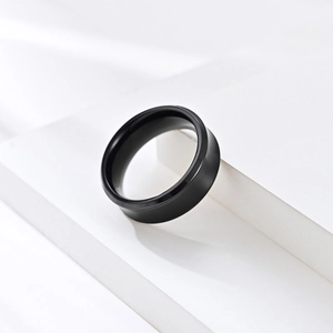 Matte black stainless steel minimalist ring with wide band on white geometric stand