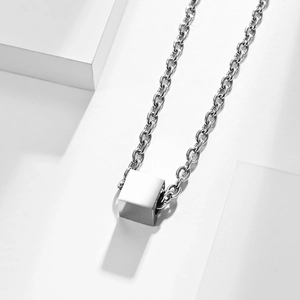 Minimalist square cube pendant necklace in polished titanium steel on stone pedestal