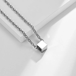 Macro detail of a silver minimalist cube pendant on O-chain over white geometric stand
