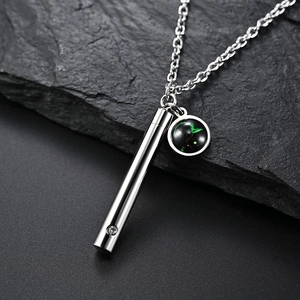 Détail macro du pendentif cylindre argenté et du charme nébuleuse sur une chaîne fine